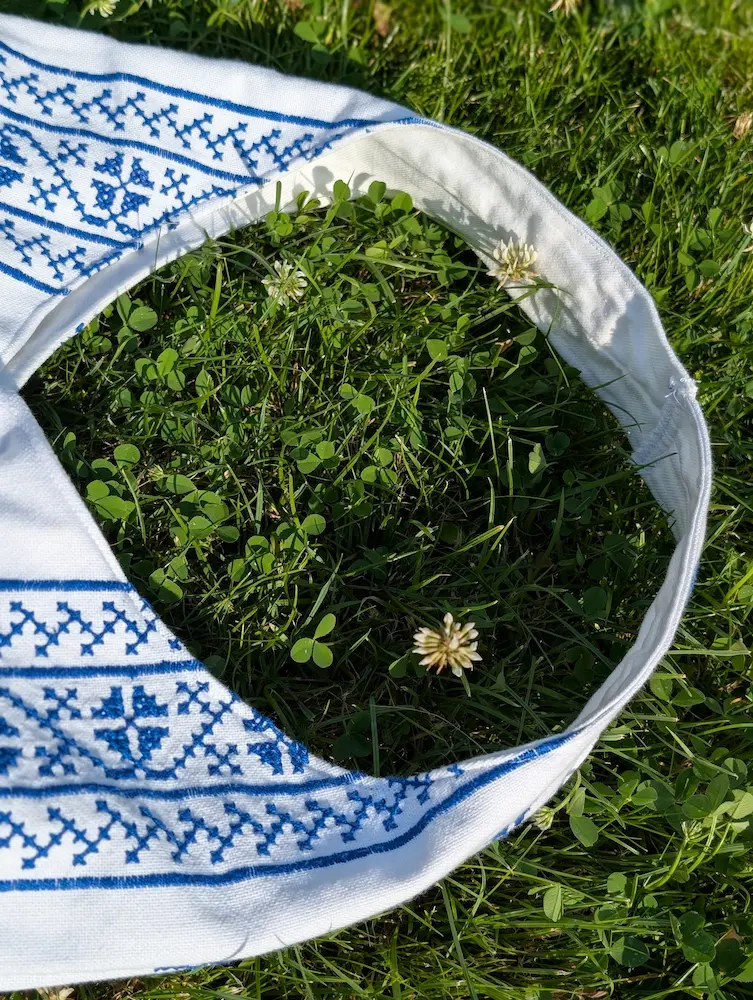 Detaliu geantă rustică din pânză albă cu flori albastre, brodate în stil tradițional, din colecția de Sânziene