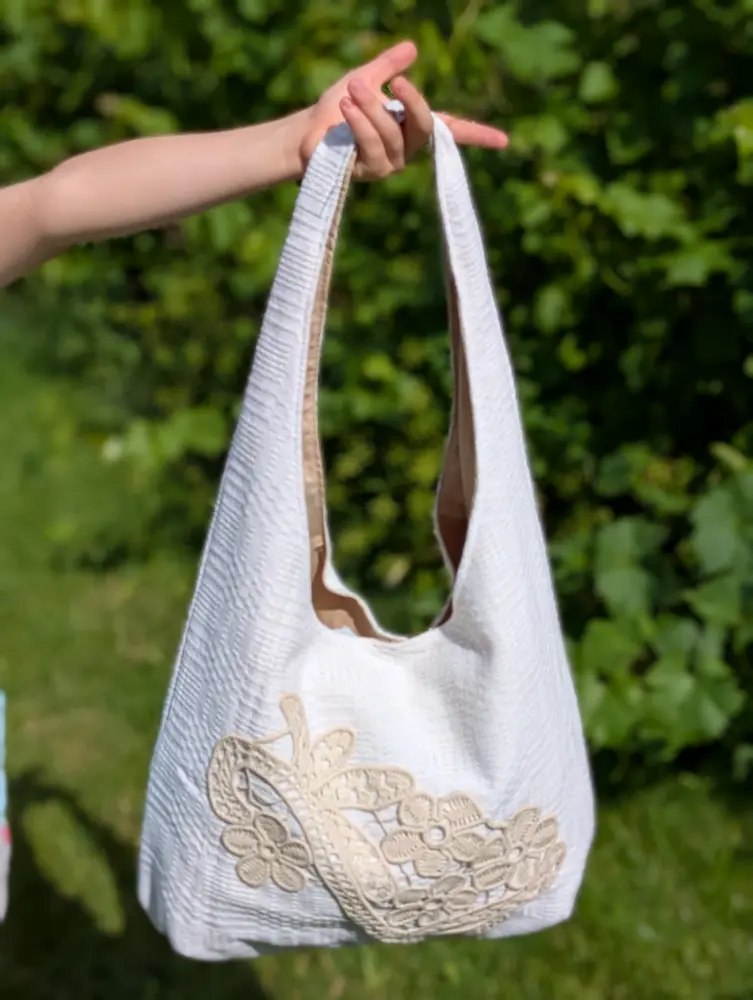 Geantă rustică din cânepă albă cu forme geometrice și dantelă cu flori bej deschis, brodate în stil tradițional, din colecția de Sânziene