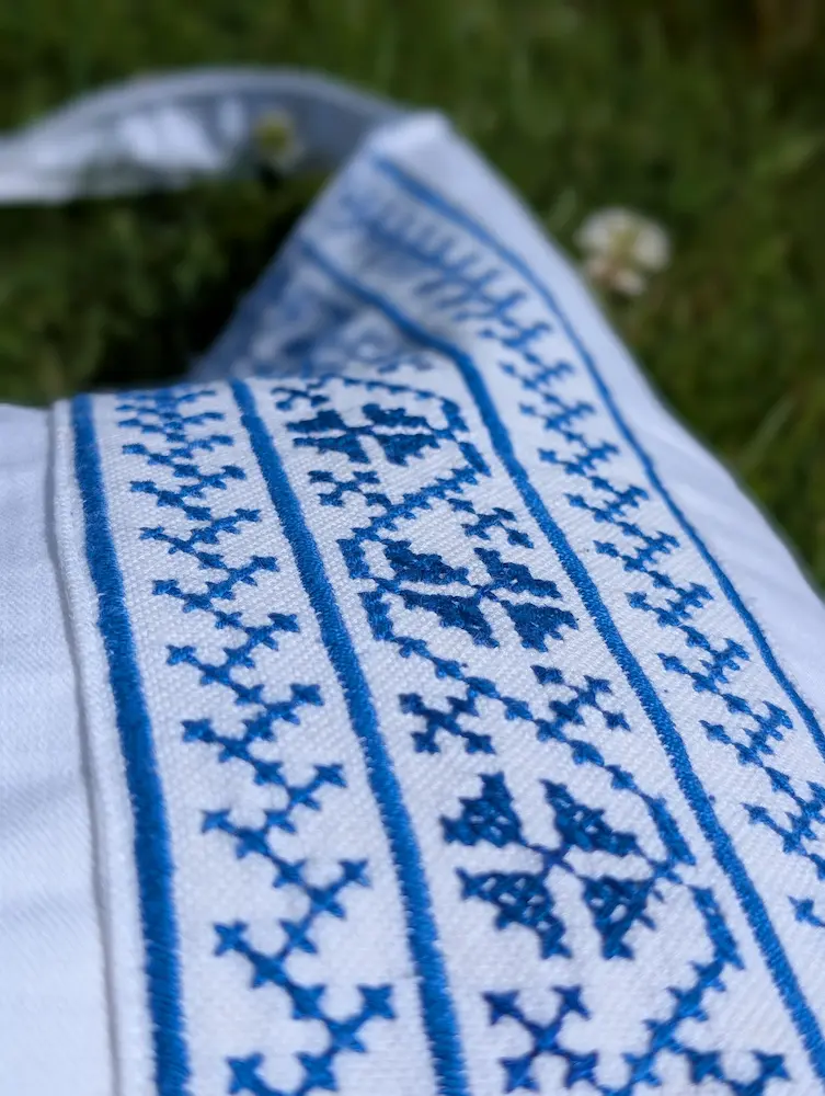 Detaliu geantă rustică din blug albastru, pânză albă cu flori albastre și motive geometrice, brodate în stil tradițional, din colecția de Sânziene