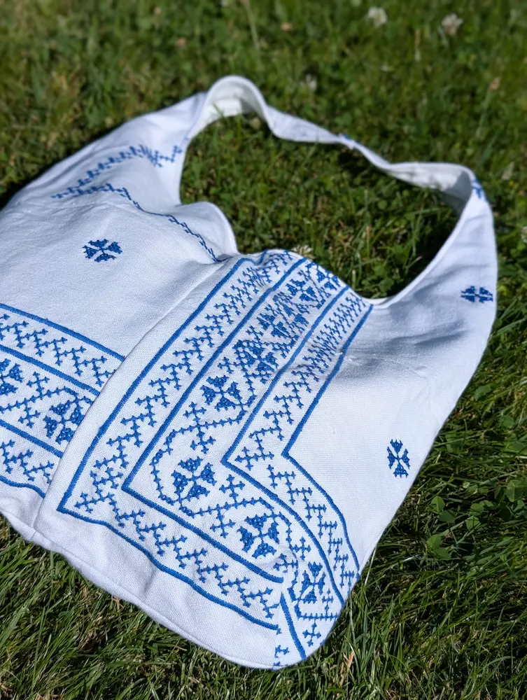Detaliu geantă rustică din pânză albă cu flori albastre și motive geometrice, brodate în stil tradițional, din colecția de Sânziene