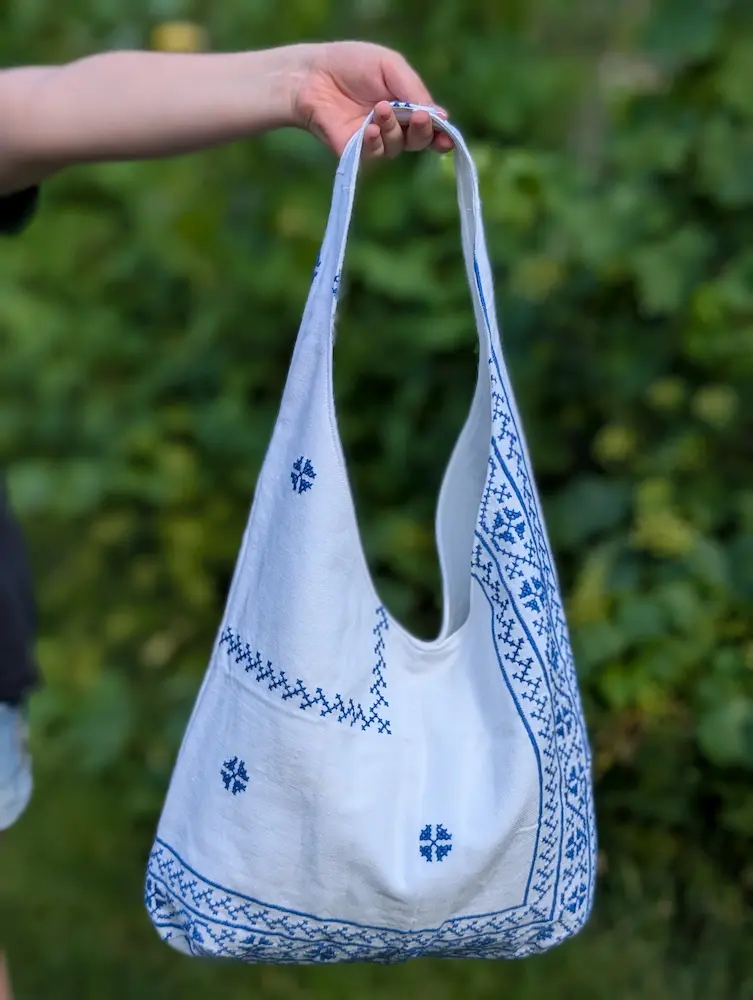 Geantă rustică din pânză albă cu flori albastre și motive geometrice, brodate în stil tradițional, din colecția de Sânziene